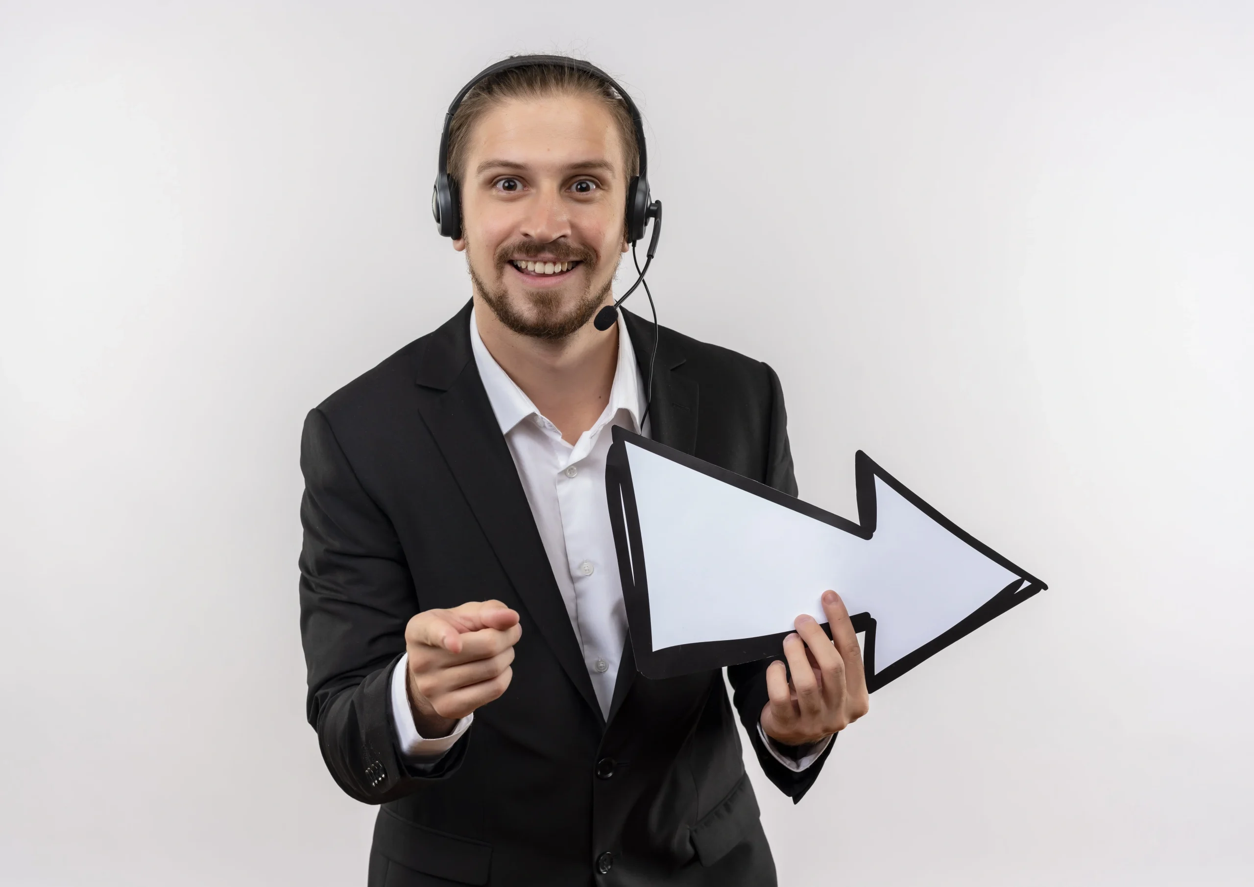 Handsome businessman suit headphones with microphone holding white arrow pointing with finger camera smiling standing white background min 1 scaled